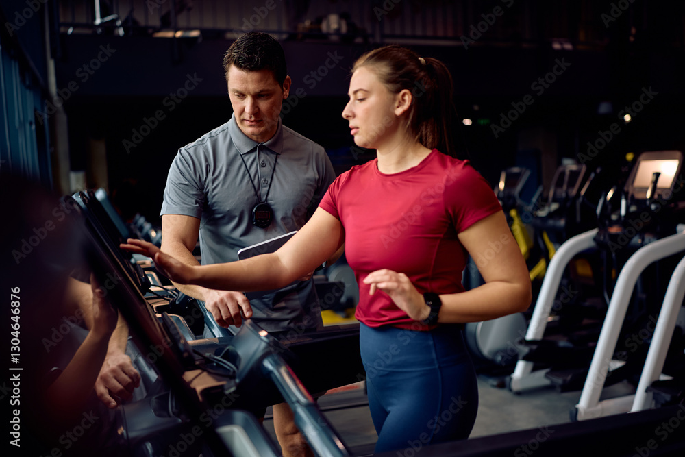 Fototapeta premium Personal trainer monitoring running of athletic woman on treadmill during sports training in gym.