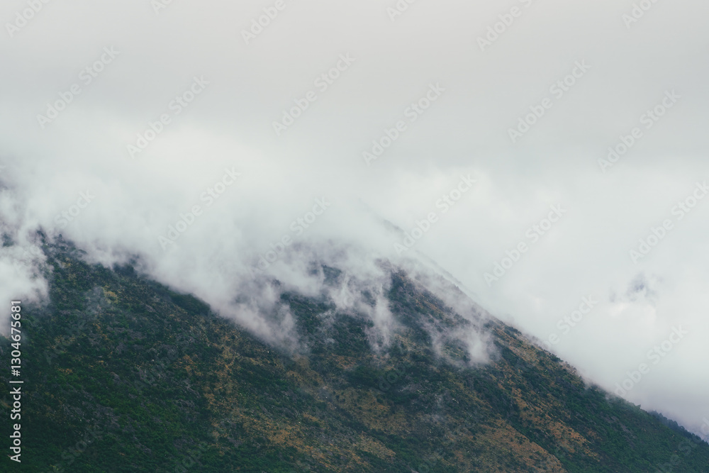 Low clouds are rising and covering the rocky mountain peaks, creating a mysterious and atmospheric landscape with lush green vegetation Low clouds are rising and covering the rocky mountain peaks, creating a mysterious and atmospheric landscape with lush green vegetation