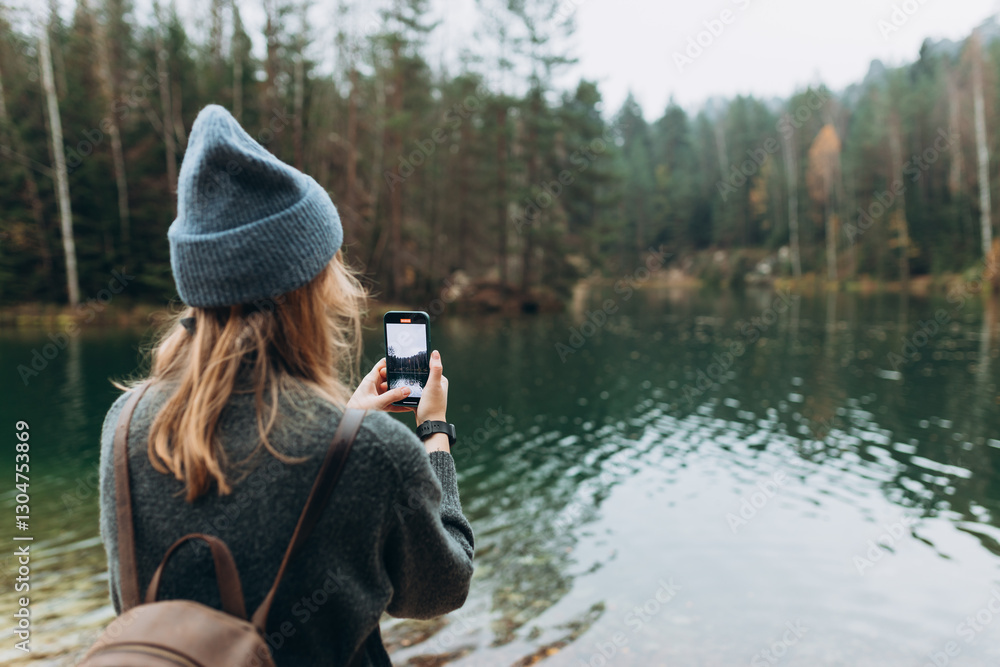 Person in hat is recording content with a smartphone near lake on wild nature background. Stylish 30s girl with phone walking outdoors. Travel, adventure. Concept of an active lifestyle. Person in hat is recording content with a smartphone near lake on wild nature background. Stylish 30s girl with phone walking outdoors. Travel, adventure. Concept of an active lifestyle.