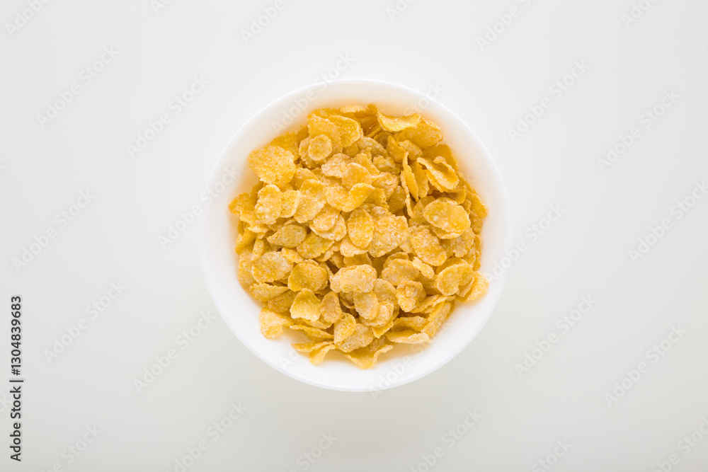 Full white bowl of yellow dry corn flakes on light gray table background. Closeup. Top down view. Full white bowl of yellow dry corn flakes on light gray table background. Closeup. Top down view.