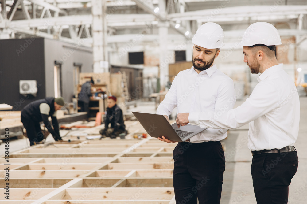 Engineers using laptop while inspecting modular building construction in factory Engineers using laptop while inspecting modular building construction in factory