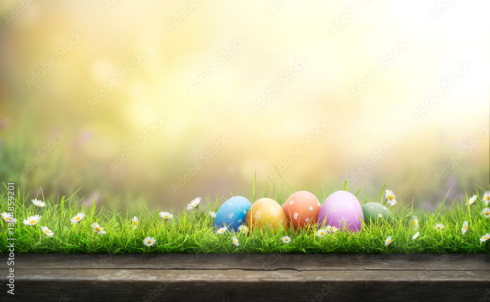 Five painted easter eggs celebrating a Happy Easter on a spring day with a green grass meadow, bright sunlight and a warm colour background with copy space and a wooden bench to display products.