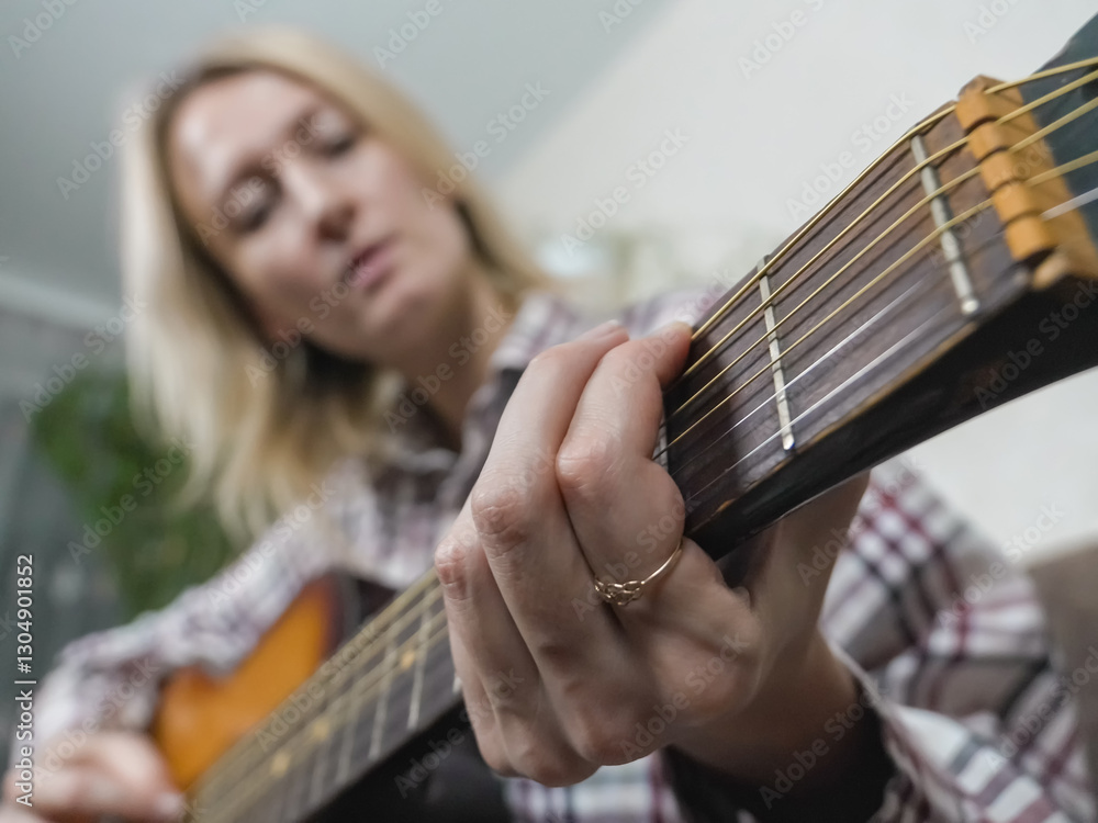 Fototapeta premium Close-up of a woman's hands skillfully playing chords on an acoustic guitar, crafting beautiful music in a cozy home setting, surrounded by a relaxed and artistic atmosphere