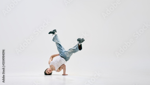 фотографія Dynamic photo of talented breakdancer balancing upside down on one hand with legs bent in air against white background