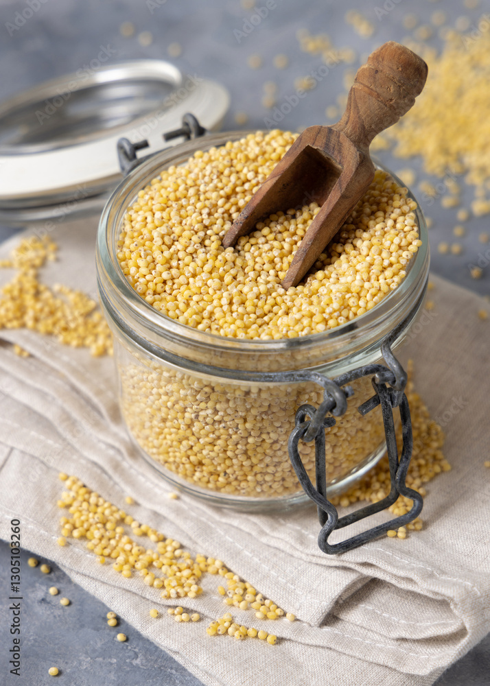 Glass jar of raw uncooked yellow millet grain with scoop on gray table closeup. Ancient food Glass jar of raw uncooked yellow millet grain with scoop on gray table closeup. Ancient food