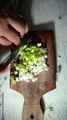 a person with hands slicing spring onions