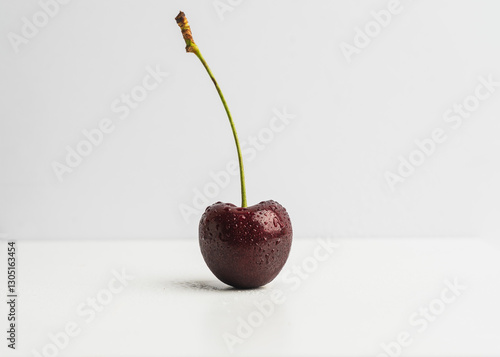 Fresh cherry with water droplets sits on a white surface against a neutral background in a simple arrangement photo