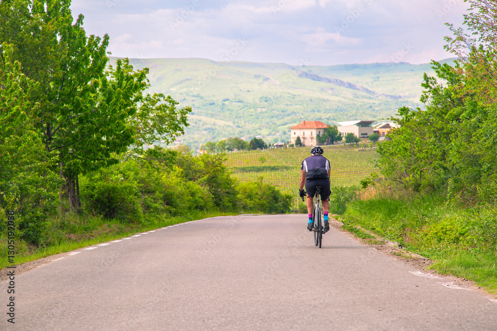 Fototapeta premium Cyclist Enjoying a Scenic Ride Through a Rural Road Surrounded by Lush Greenery and Hills