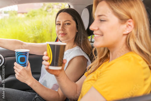 Obraz na płótnie Two women sitting in a car, holding takeaway coffee cups and enjoying a friendly conversation, radiating a warm and relaxed atmosphere. w salonie