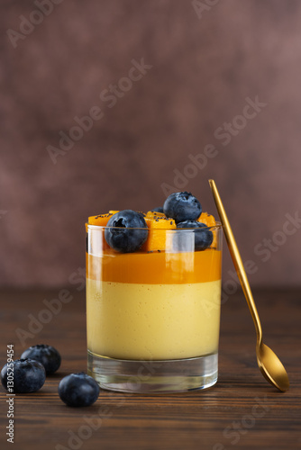 Vegan mango panna cotta mousse pudding with blueberries on a wooden table. Sugar, lactose and sugar substitutes free. Vertical orientation.