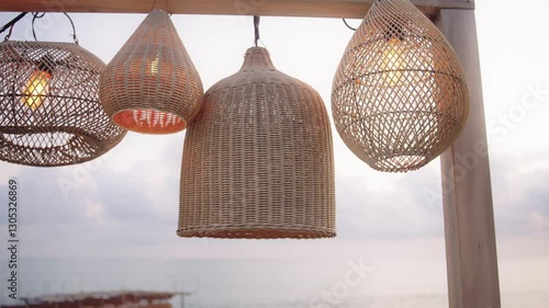 Cozy wicker lamps hanging at seaside terrace with ocean view. Natural decor, tropical design, summer evening atmosphere by the sea.