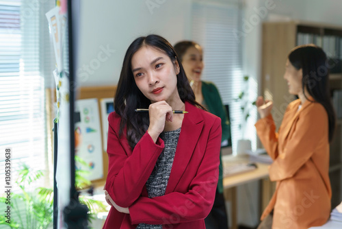 Vászonkép Professional Asian businesswoman wearing red suit, pondering while holding pen,