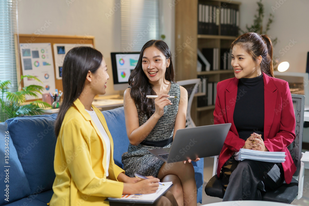 Three asian businesswomen are smiling and discussing strategy during a meeting in a modern office, using a laptop and taking notes on documents Three asian businesswomen are smiling and discussing strategy during a meeting in a modern office, using a laptop and taking notes on documents