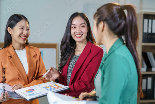 Wallpaper Mural Three young businesswomen are smiling and discussing financial report during a meeting in a modern office, showing teamwork and collaboration Torontodigital.ca