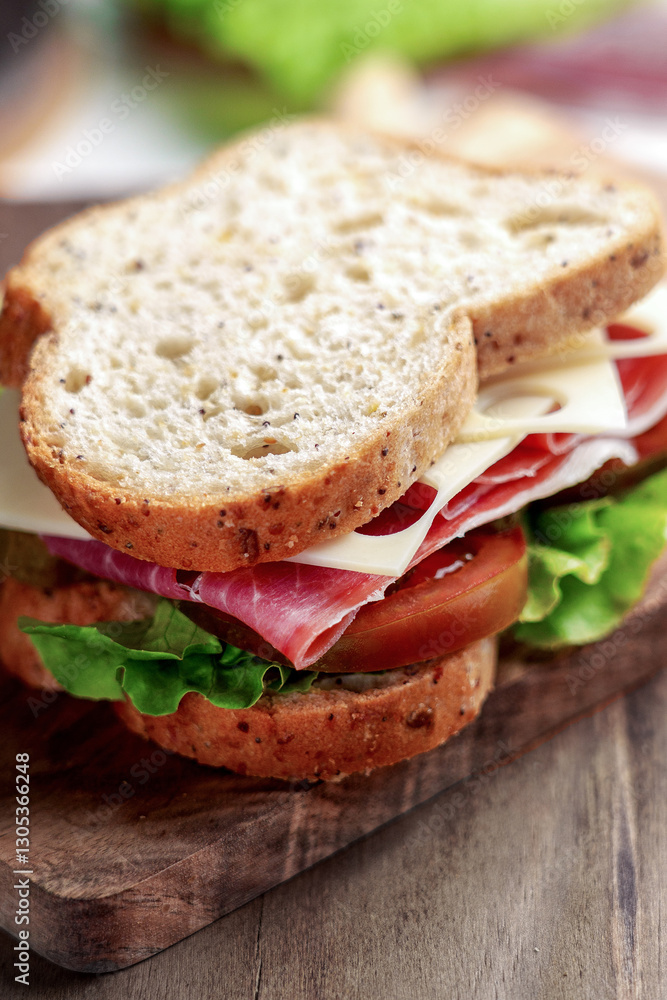 Whole grain bread sandwich with cured ham, Kumato tomato, Swiss cheese and fresh lettuce on a wooden board Whole grain bread sandwich with cured ham, Kumato tomato, Swiss cheese and fresh lettuce on a wooden board