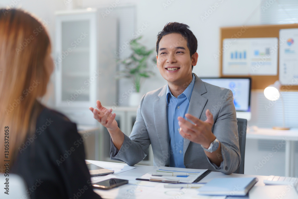 Asian businessman gesturing with hands while engaging in discussion with colleague in office during business meeting, explaining graphs and charts to illustrate strategies and insights Asian businessman gesturing with hands while engaging in discussion with colleague in office during business meeting, explaining graphs and charts to illustrate strategies and insights
