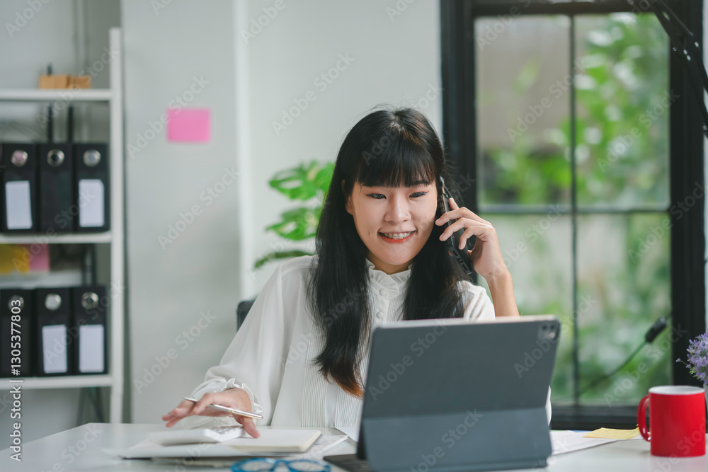 Professional female executive speaking on smartphone, reviewing digital tablet while seated at sleek workspace, embodying contemporary corporate efficiency and concentration Professional female executive speaking on smartphone, reviewing digital tablet while seated at sleek workspace, embodying contemporary corporate efficiency and concentration
