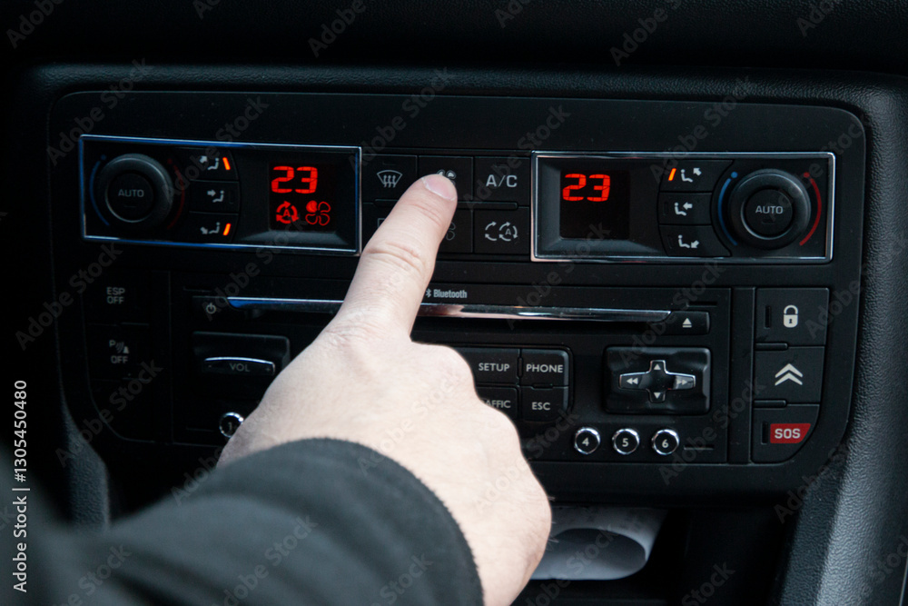 Fototapeta premium Hand pointing at dual-zone climate control on a car dashboard, showcasing advanced automotive features and comfort.