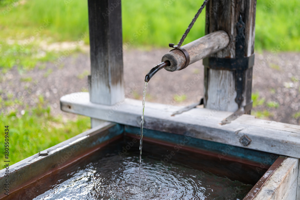 Close-up of an old wooden pump with water flowing into a trough. The rustic charm of this vintage pump evokes nostalgia for simpler times and traditional water systems