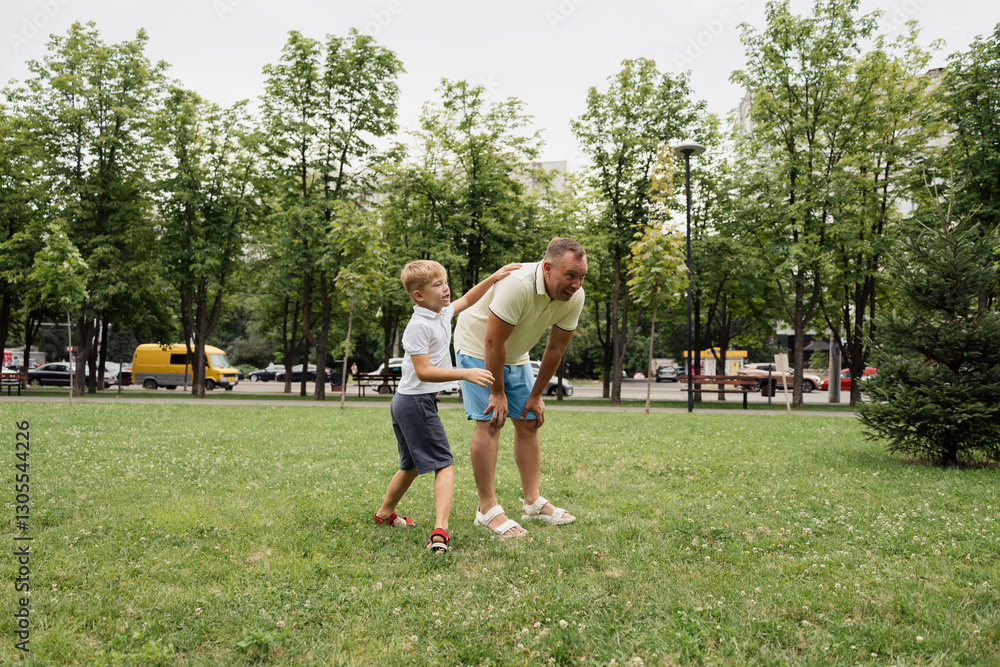 Father and son enjoying a playful moment in the park. Happy outdoor time together, featuring green trees and a grass field. Father and son enjoying a playful moment in the park. Happy outdoor time together, featuring green trees and a grass field.
