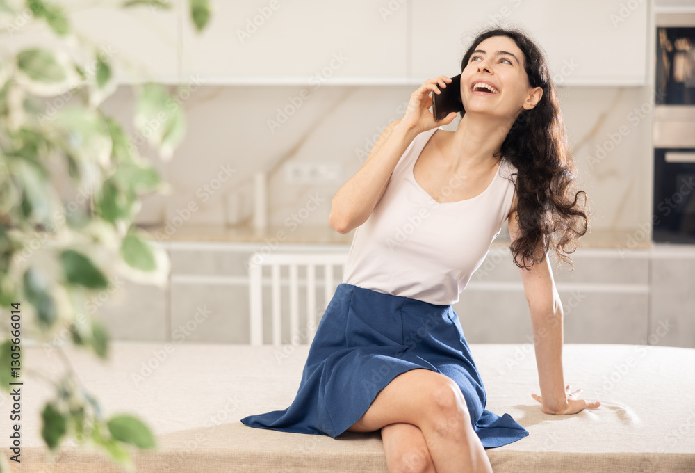 Joyful woman talking on smartphone while sitting on kitchen table Joyful woman talking on smartphone while sitting on kitchen table
