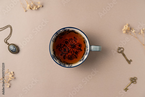 Cup of tea with vintage medallion, keys and flowers on beige background from above. Flat lay, top view.