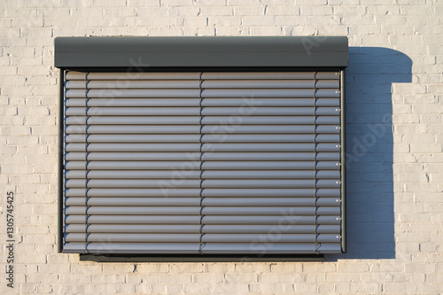 Modern window with closed horizontal metal roller shutters installed on a white brick wall