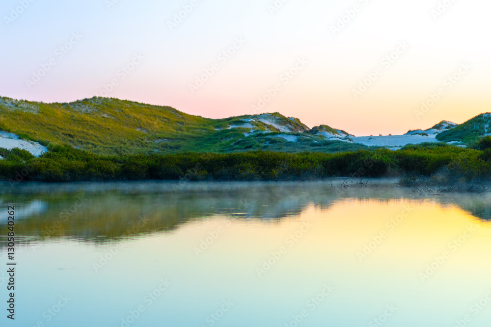 Tranquil sunset reflection over calm water surrounded by lush greenery and rolling sand dunes Tranquil sunset reflection over calm water surrounded by lush greenery and rolling sand dunes