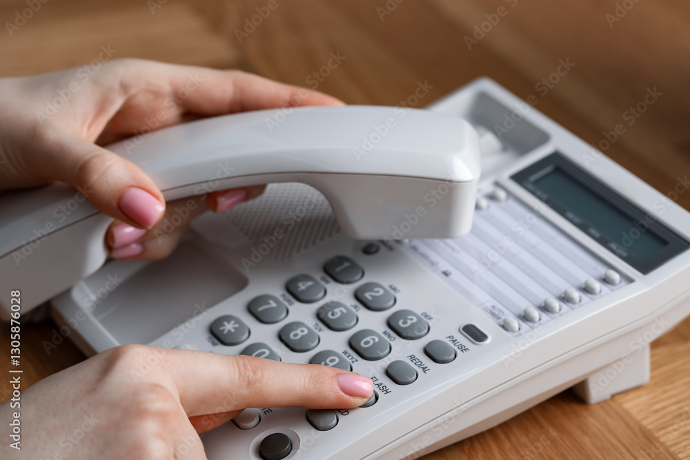 Woman dialing number on telephone at wooden table, closeup Woman dialing number on telephone at wooden table, closeup