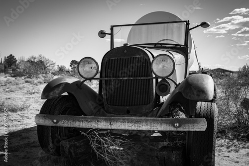 An antique Model A truck hauling a large tank in the desert. Black and white.