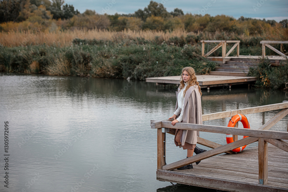 A blonde model girl walks along the pier against the background of the lake A blonde model girl walks along the pier against the background of the lake