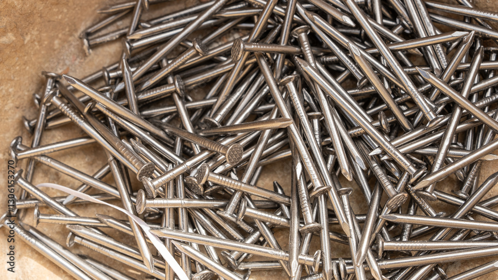 A close-up shot of a pile of shiny steel nails scattered on a rough surface. The metallic texture, sharp points, and grooved heads highlight construction materials used in carpentry and building. A close-up shot of a pile of shiny steel nails scattered on a rough surface. The metallic texture, sharp points, and grooved heads highlight construction materials used in carpentry and building.