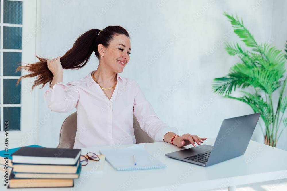 Brunette businesswoman sitting at desk in office with educational books online Brunette businesswoman sitting at desk in office with educational books online