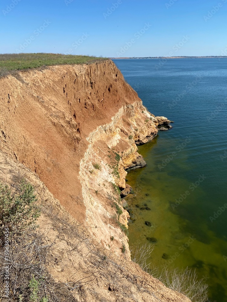 Obraz premium A rocky cliff above a river with a gentle yet steep slope, almost a drop-off. The entire scene is evenly illuminated by sunlight, highlighting the natural beauty of the landscape.