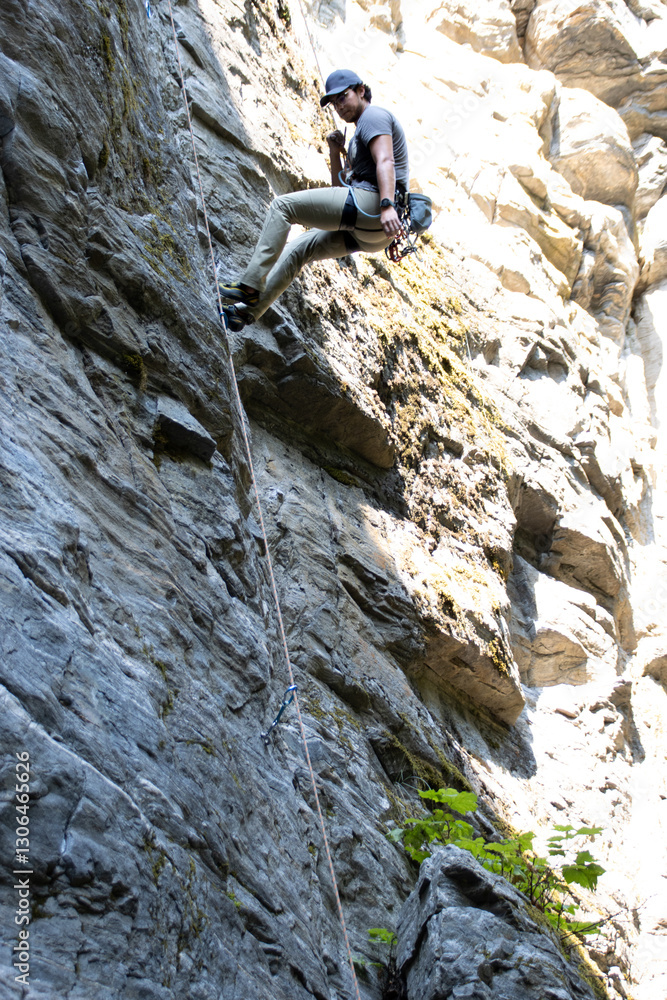 A rock climber descends rock face using climbing gear and ropes A rock climber descends rock face using climbing gear and ropes