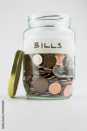 A glass jar containing coins with a handwritten label BILLS against a white background. The concept is to show small amounts of money being kept separately for use against a specific outcome.
