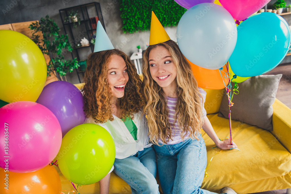 Obraz premium Two young girls enjoying a festive weekend at home with vibrant balloons and party hats, expressing joy and friendship