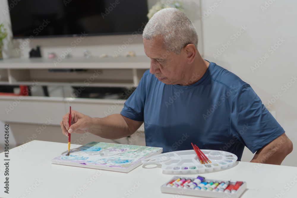Senior man painting on canvas at home using a brush and watercolor paints Senior man painting on canvas at home using a brush and watercolor paints