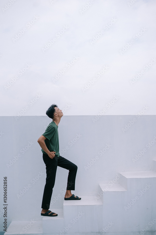 Aspiring young man climbing minimalist white stairs looking ahead Aspiring young man climbing minimalist white stairs looking ahead