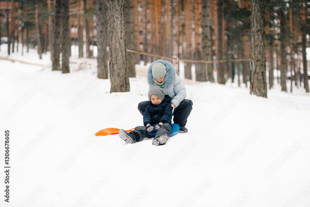 Mother helping son getting ready to ride snow sled in snowy forest Mother helping son getting ready to ride snow sled in snowy forest