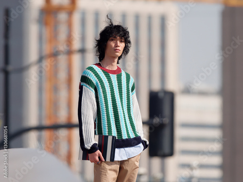 Portrait of handsome Chinese young man with striped sweater walking in the street, young guy with black curly hair with urban background. male fashion, cool Asian young man lifestyle.