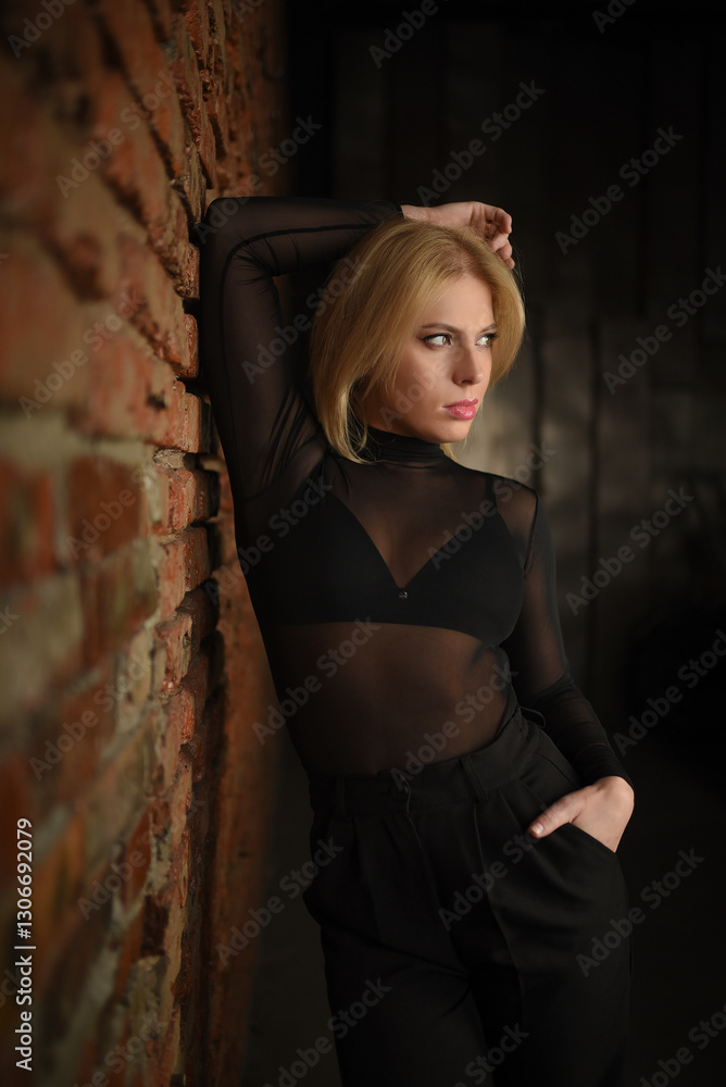 Fototapeta premium A beautiful blonde woman in a black bodysuit and pants posing near a brick wall.