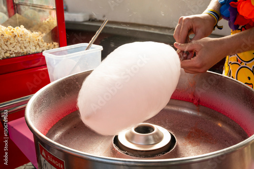 A person is making cotton candy. The cotton candy is being made in a machine. The machine is silver and red photo