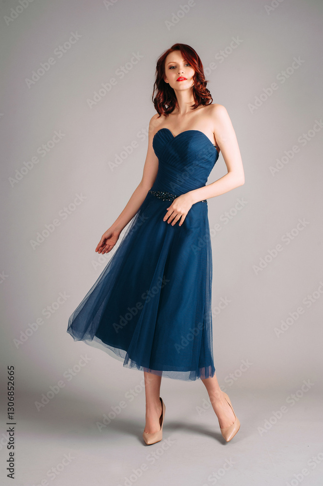 Fototapeta premium Sexy young redhead woman dancing in studio, romantic portrait. Deep blue sweetheart neckline midi dress. Corset sleeveless classic evening gown, festive outfit.Touching look for an event, flying skirt