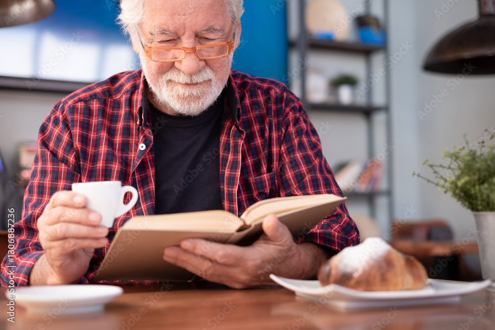 Smiling relaxed senior bearded man sitting at cafe table reading a book enjoying breakfast with coffee and croissant. Elderly caucasian male in eyeglasses and checkered shirt Smiling relaxed senior bearded man sitting at cafe table reading a book enjoying breakfast with coffee and croissant. Elderly caucasian male in eyeglasses and checkered shirt