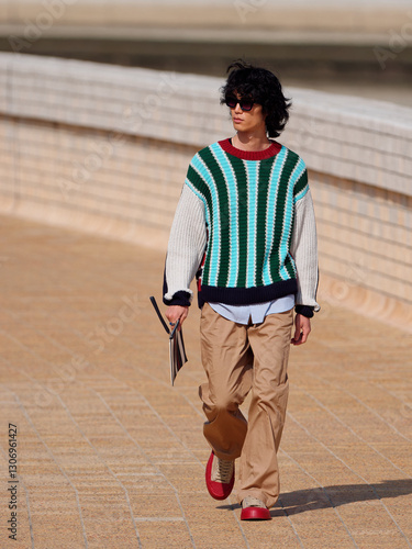 Portrait of handsome Chinese young man with striped sweater walking in the street, young guy with black curly hair with urban background. male fashion, cool Asian young man lifestyle.