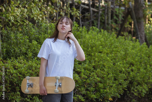 Portrait of teenage girl holding skateboard in white t-shirt with her hair down on green background.