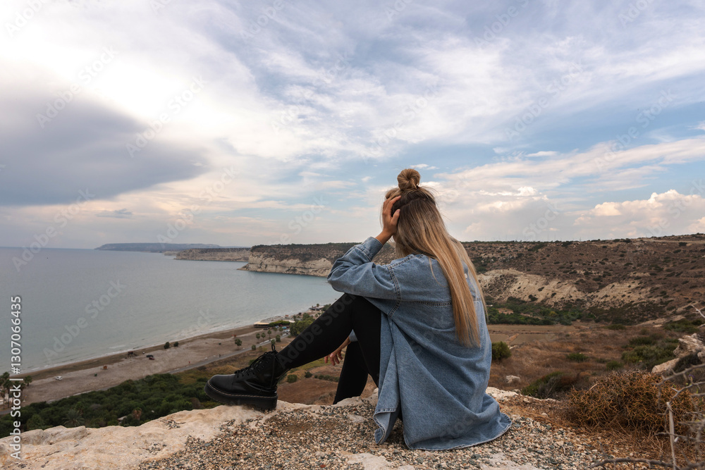 Young Woman Enjoying Peaceful Coastal View from a Cliff Young Woman Enjoying Peaceful Coastal View from a Cliff