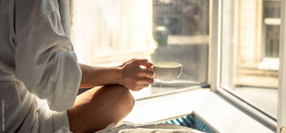 Fototapeta premium Woman in white bathrobe lying on sofa and relaxing with cup of tea at home.