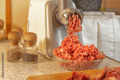 Minced meat comes out of the meat grinder and falls into a glass plate. Cooking photo